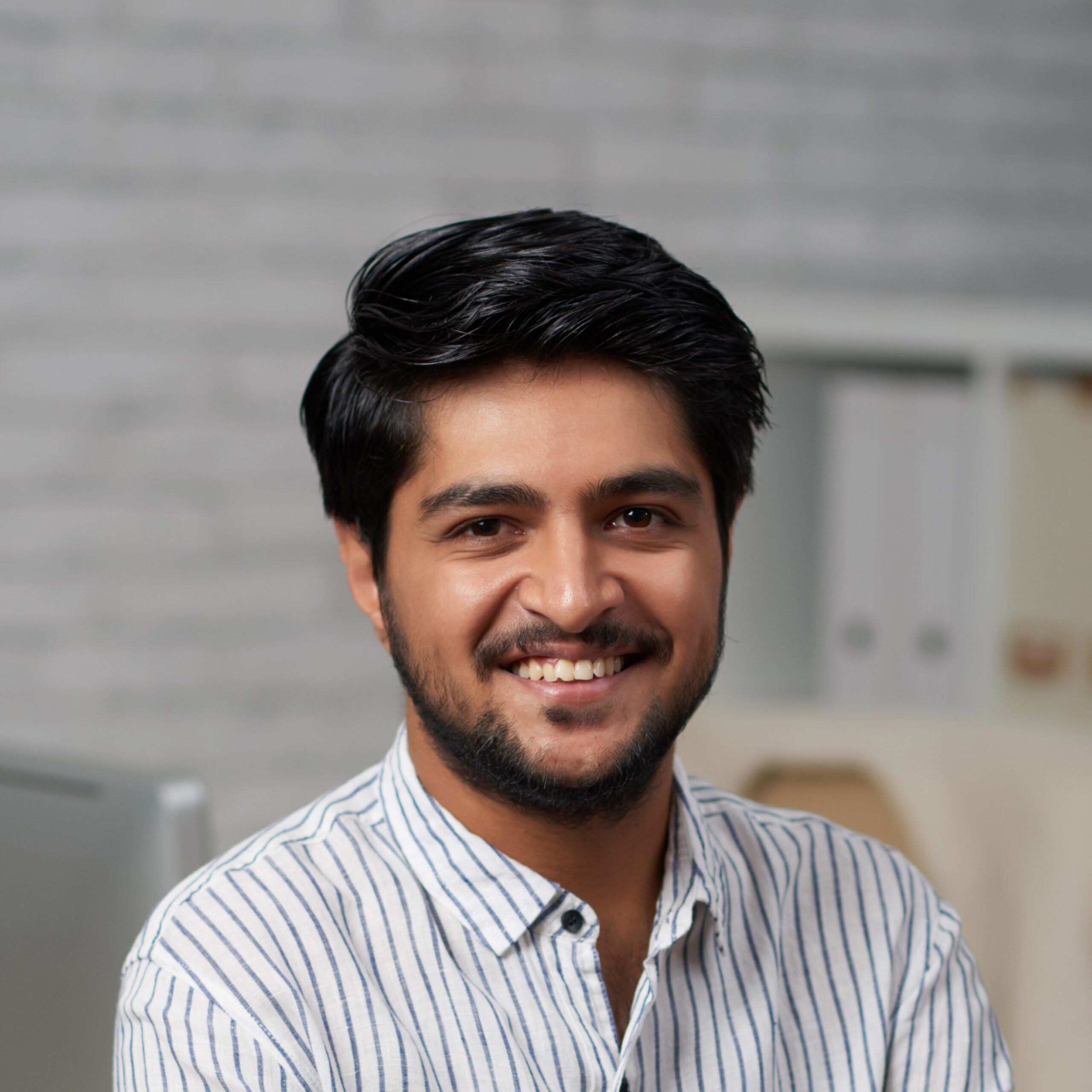 Confident young Indian businessman sitting on edge of his table and looking at camera