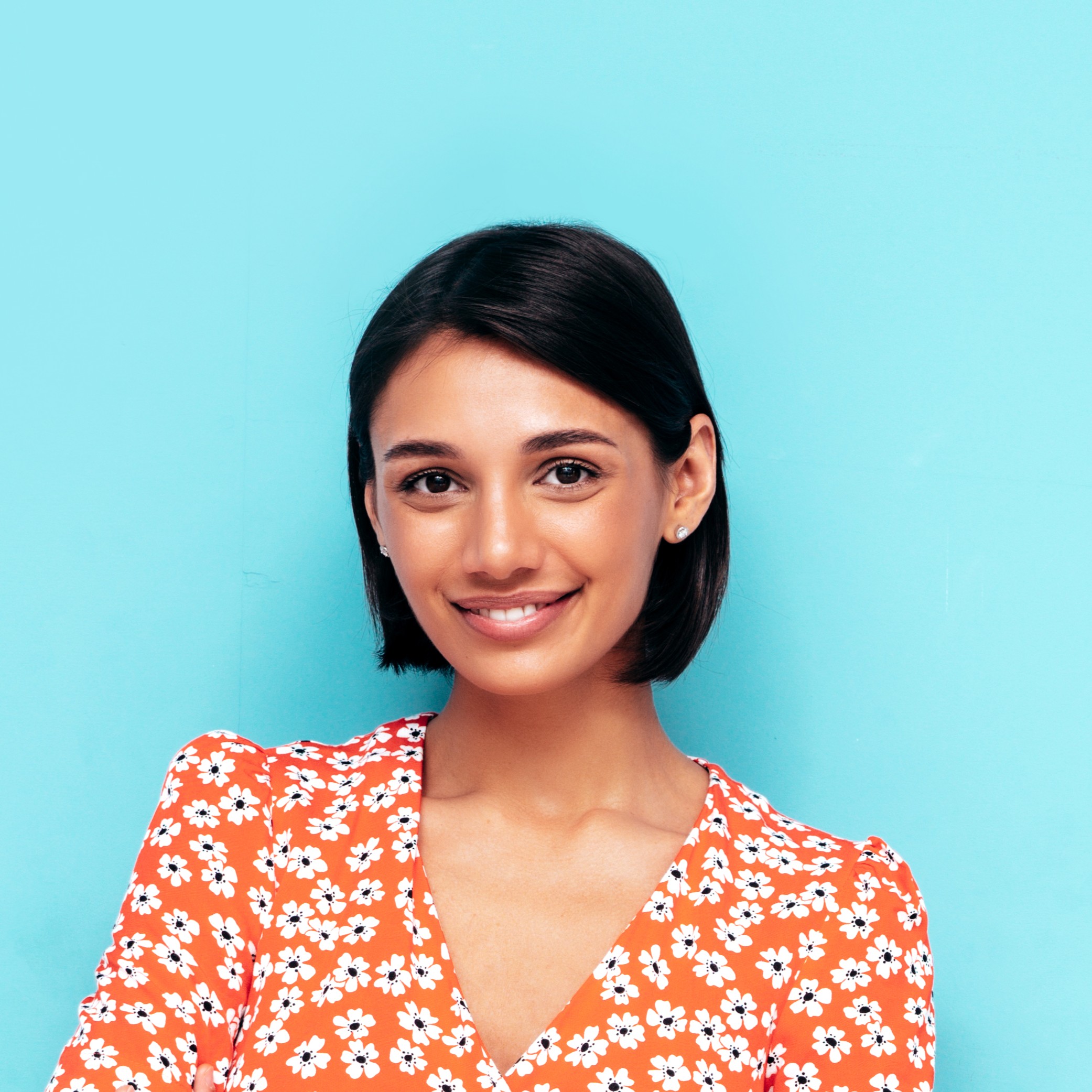Young beautiful smiling female in trendy summer red dress. Sexy carefree woman posing near blue wall in studio. Positive model having fun. Cheerful and happy. Isolated. Crossed arms